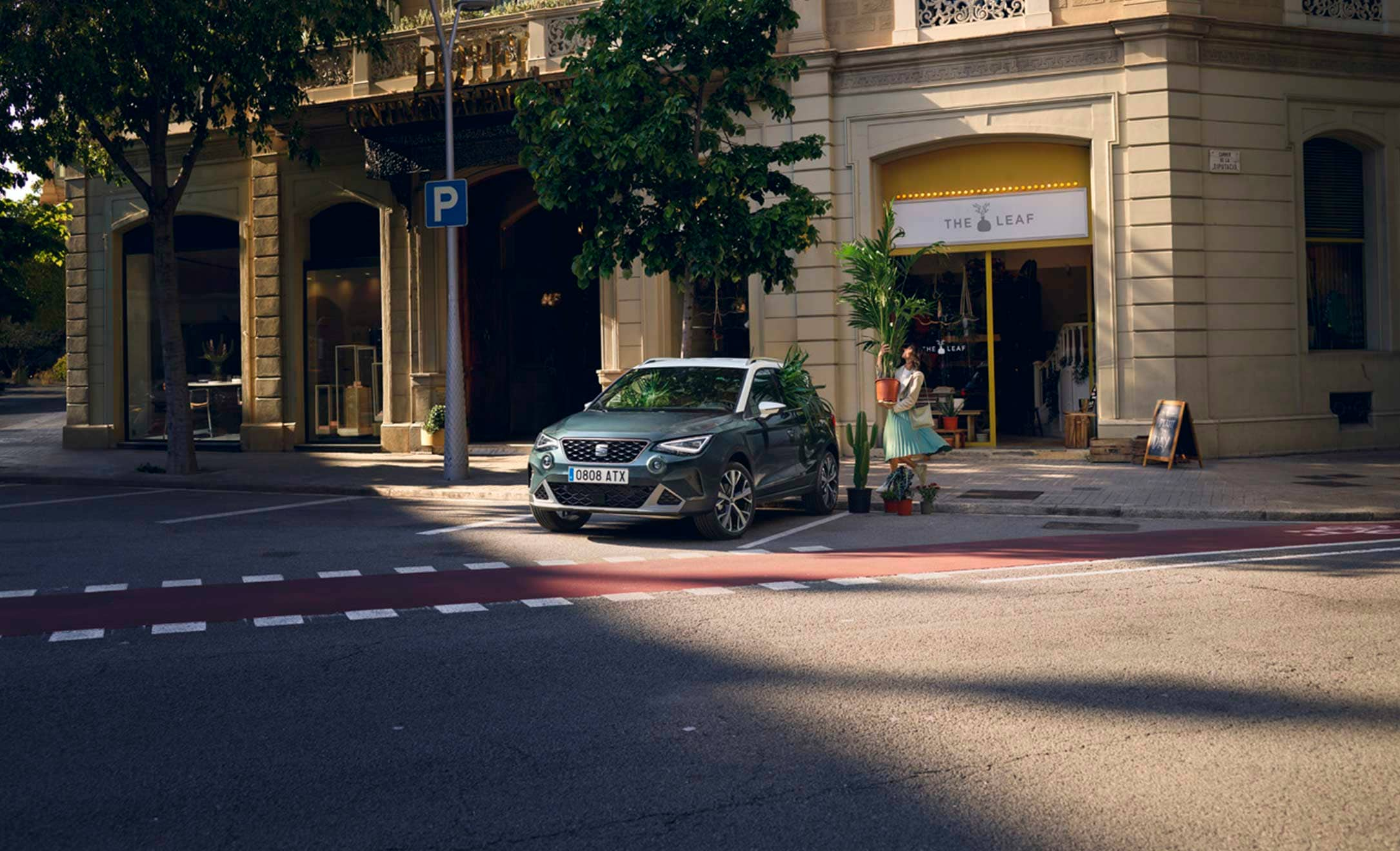 Woman walking to put a plant inside a SEAT Arona dark camouflage colour with candy white roof 